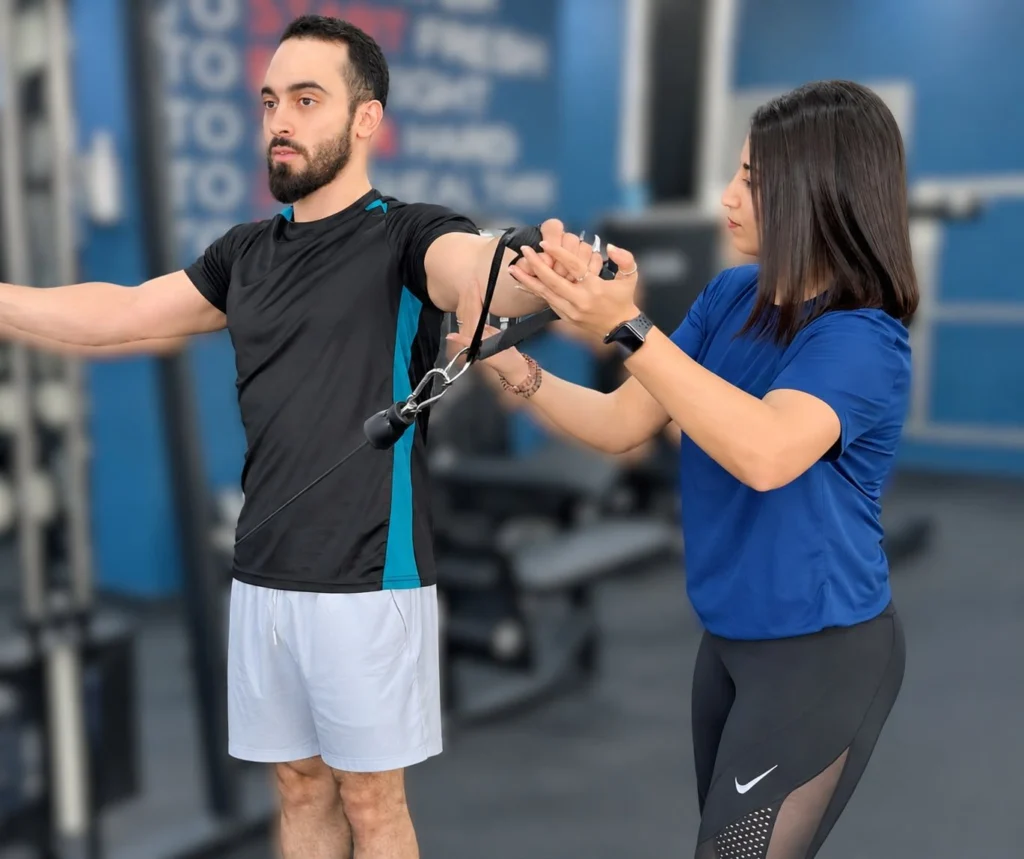 Trainer correcting shoulder form on a cable exercise