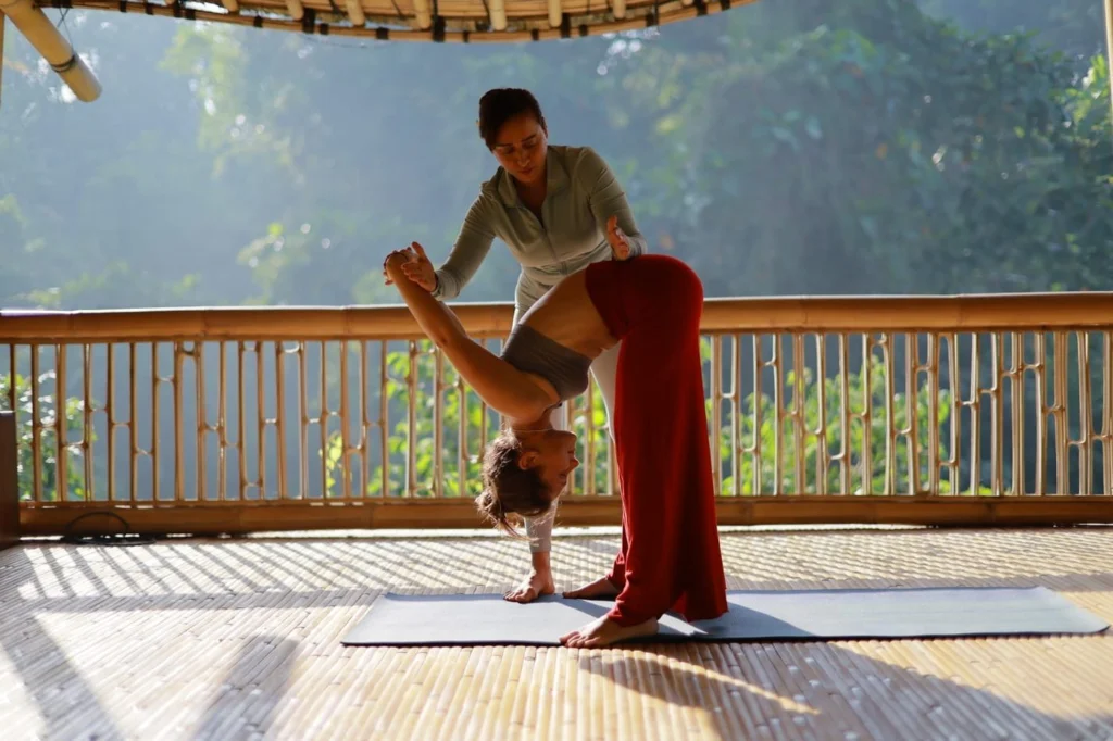 Yoga instructor assisting a client with a deep forward stretch